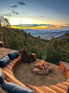 a man sitting in front of a fire pit at Wagon Cella Faroeste Acima das Nuvens Spa Ofurô Aquec Campos do Jordão in Campos do Jordão
