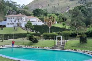 una persona parada junto a una piscina frente a una casa en Pousada Sítio São Luiz - Café da Manhã Piscina - Petrópolis, en Petrópolis