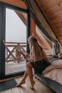 eine Frau, die auf einem Bett sitzt und ein Buch liest in der Unterkunft Domki Osada Zieleniec in Duszniki-Zdrój + 73 Fotos