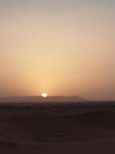 a sunset in the desert with the sun in the horizon at Erg Camp Merzouga in Merzouga