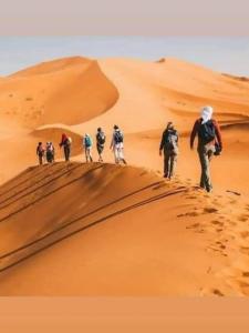 a group of people walking on a sand dune at Erg Camp Merzouga in Merzouga