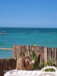 a beach with a chair and the ocean with boats at Casa da Peroba Sol - Pé na Areia - Praia da Peroba - Icapuí in Icapuí