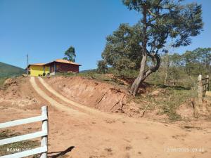 une maison sur un chemin de terre avec une clôture et un arbre dans l'établissement Chalé Arminda Costa, à Ouro Preto