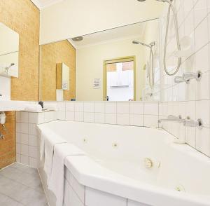 een witte badkamer met een bad en een spiegel bij Cranbourne Motor Inn in Cranbourne