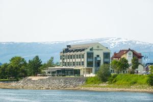 a building next to a river with mountains in the background at Fru Haugans Hotel in Mosjøen