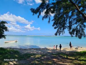 a group of people walking on a beach with a boat at Jugroop Beach House in Baie du Tombeau