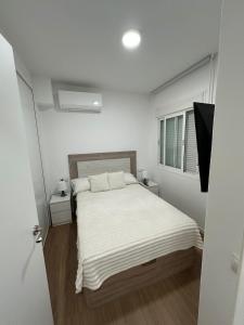 a white bedroom with a bed and a window at Apartamentos JM - Sea & Sun in Roquetas de Mar