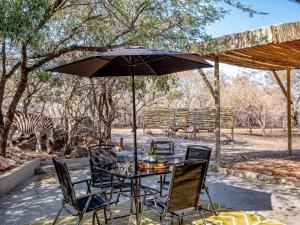 a table and chairs with an umbrella and a zebra at Little Orvyll's in Marloth Park