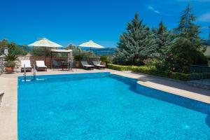 a blue swimming pool with chairs and umbrellas at Pirofani Villa Apartments in Apolpaina