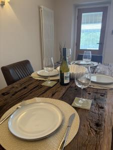 ein Holztisch mit weißen Tellern und Weingläsern in der Unterkunft Sunset Cottage - 55 South Lane in Holmfirth