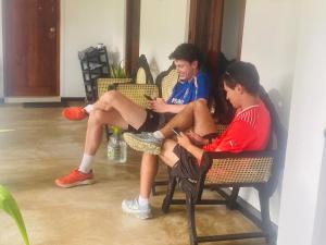 two young men sitting on wicker chairs looking at their cell phones at Ella Mount Hostel in Ella