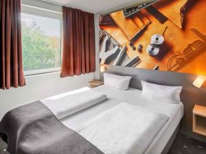 Un dormitorio con una gran cama blanca y una ventana. en B&B Hotel Offenbach-Süd, en Offenbach