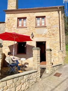 a man sitting in a chair under an umbrella in front of a stone house at The Cliffs - Casa Crecide in O Vicedo