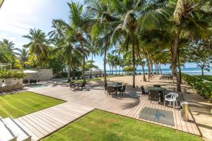 Un patio con mesas y sillas y palmeras. en Beachfront 4beds Jacuzzi Privacy Full Kitchen, en La Puntica de Juan Dolio
