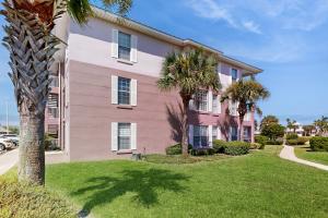 una casa rosa con palme di fronte di Coastal condo with pool, lanai, washer/dryer, & elevator a Saint Augustine Beach