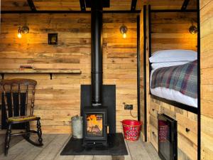 a fireplace in a wooden cabin with a bed at Shepherd's Huts at Cotswold Hills Country Park in Chipping Norton