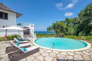 a swimming pool with chairs and an umbrella next to a house at Hospitality Expert HALF HILL Pool Beach in Montego Bay