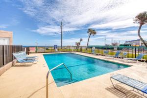 a swimming pool with chairs and the ocean in the background at Beach Dont My Vibe in Ormond Beach
