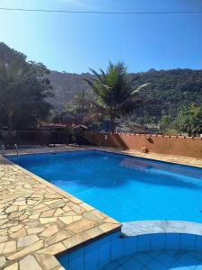 a large blue swimming pool with palm trees in the background at Chalé Residencial Bosque da Cocanha in Caraguatatuba