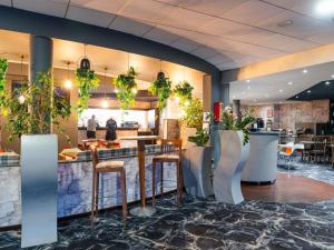 a restaurant with a bar with stools and plants at Novotel Milton Keynes in Milton Keynes