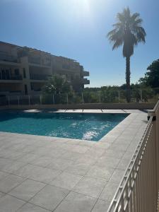 a swimming pool in front of a building with a palm tree at Appartement proche mer in Le Muy