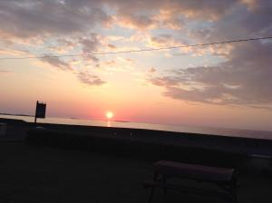 un banco frente a una puesta de sol en la playa en Seaside Chalet en Quilty