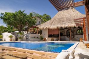 a swimming pool with a straw umbrella and a house at Pelican Eyes Hotel and Resort in San Juan del Sur