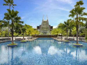 a swimming pool in front of a building with palm trees at Novotel Palembang in Palembang