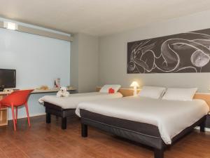 a room with two beds and a desk and a tv at ibis La Bresse Gérardmer in La Bresse