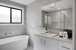 a white bathroom with a tub and a sink at Ahgunyah Beach House in Mollymook +18 photos