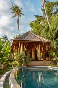 a resort with a swimming pool and a thatch hut at Rumah Kita Ecolodge in Ubud