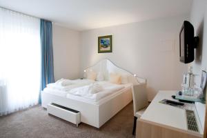 Habitación blanca con cama blanca y escritorio. en Frühstückshotel Seemannsbraut Amrum - adults only, en Wittdün