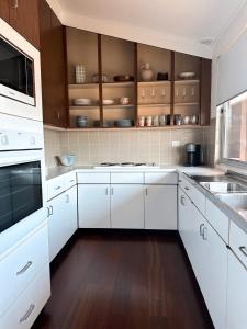 Una cocina blanca con pisos de madera y gabinetes blancos. en One Mile Horizon - Beach House, en Forster