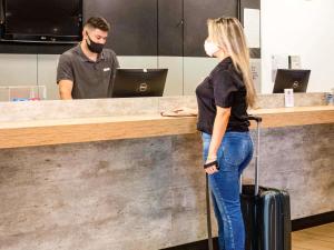 a woman in a mask standing at a counter with her luggage at ibis Santos Gonzaga Praia in Santos +61 photos