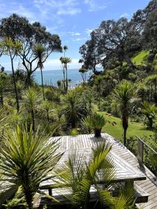 a garden with a table and palm trees and the ocean at Whananaki Hideaway in Whananaki
