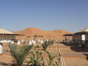 a desert area with buildings and trees and mountains at ChariF Luxury Camp in Rissani