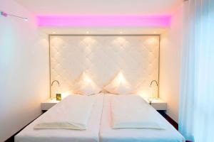 a bedroom with a large white bed with pink lighting at Mintrops Land Hotel Burgaltendorf in Essen