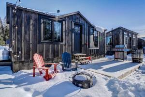 a cabin with two chairs and a table in the snow at Your Cozy Cabin Retreat in Saint-Rémi-dʼAmherst