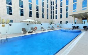 a large swimming pool with chairs and a building at Premier Inn Doha Education City in Doha +21 photos