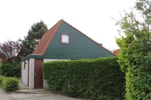 a small house with a green roof and a hedge at Het Coraaltje in Julianadorp