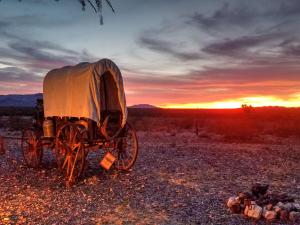 Vagón acorazado en medio de un campo con una puesta de sol en Stagecoach Trails Guest Ranch, en Yucca