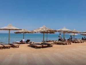 a beach with tables and straw umbrellas and the ocean at 2 Bedroom Chalet pool& sea view just steps from the sea fanar de luna ain sokhna in Ain Sokhna