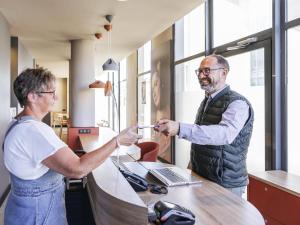 a man handing a woman something at a desk at ibis Styles Le Mans Gare Sud in Le Mans