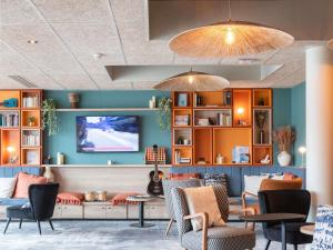 ibis Bayeux Port En Bessin في بورت-أون-بيسين-هوباين: منطقة انتظار مع كراسي وطاولات وتلفزيون