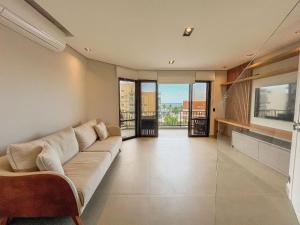 a living room with a couch and a large window at Cobertura Pé na Areia - Enxoval Completo Riviera in Riviera de São Lourenço