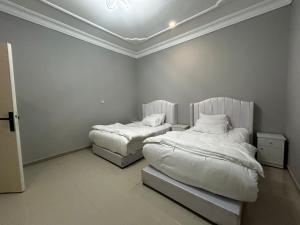 Habitación con 2 camas, sábanas blancas y techo. en شقة الزهور, en Al Nairyah