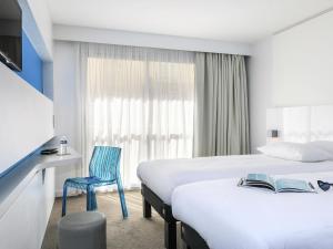 a hotel room with two beds and a blue chair at Ibis Styles Menton Centre in Menton
