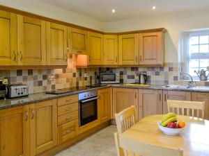 a kitchen with wooden cabinets and a table with a bowl of fruit at Maesbangor Farmhouse in Capel Bangor +25 photos