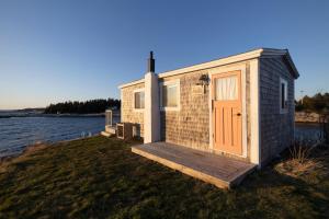a small house with a wooden porch next to a body of water at Starfish Cottage in Peggy's Cove
