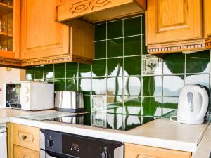 a kitchen with wooden cabinets and green tiles on the wall at The Chalet - Uk34712 in Reighton